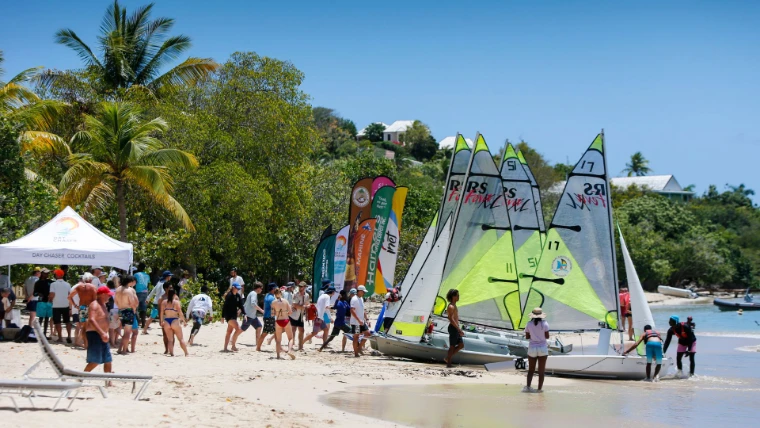 Sailors running up the beach to their dinghies beneath the palms at the beach race at Antigua Sailing Week, a late-April engagement in the season calendar of The Mansa Court