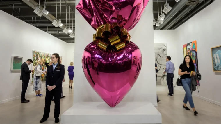 A polished magenta heart sculpture tied with a gold bow, visitors moving among the gallery stands at Art Basel, a mid-June engagement in the season calendar of The Mansa Court