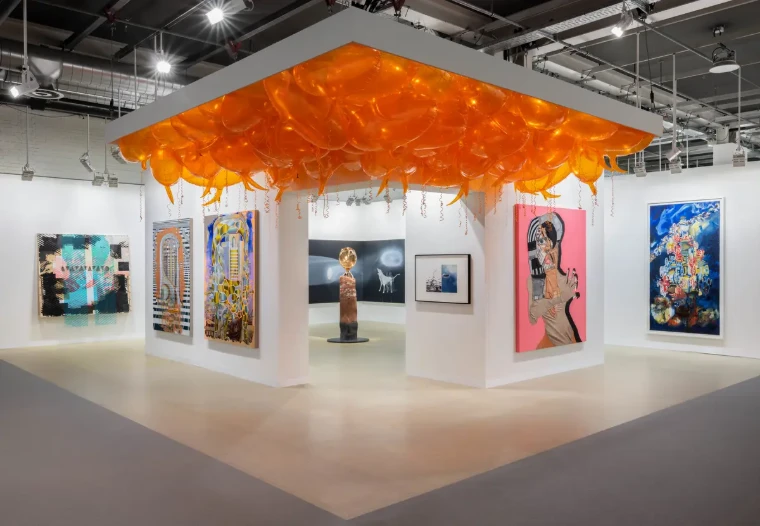 A gallery stand hung with paintings beneath a ceiling of orange balloons at Art Basel in Messe Basel, a mid-June engagement in the season calendar of The Mansa Court