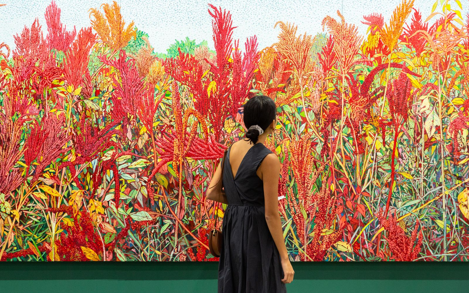 A visitor standing before a large red and green painting at Art Basel Hong Kong, the Asian art fair kept in The Mansa Court calendar