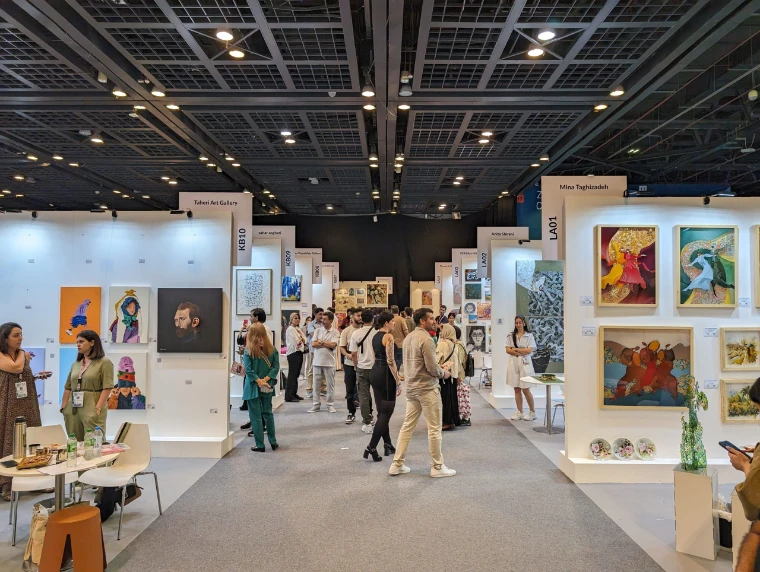 Visitors along an aisle of gallery stands hung with paintings during Dubai’s spring art week, a mid-April engagement in the season calendar of The Mansa Court