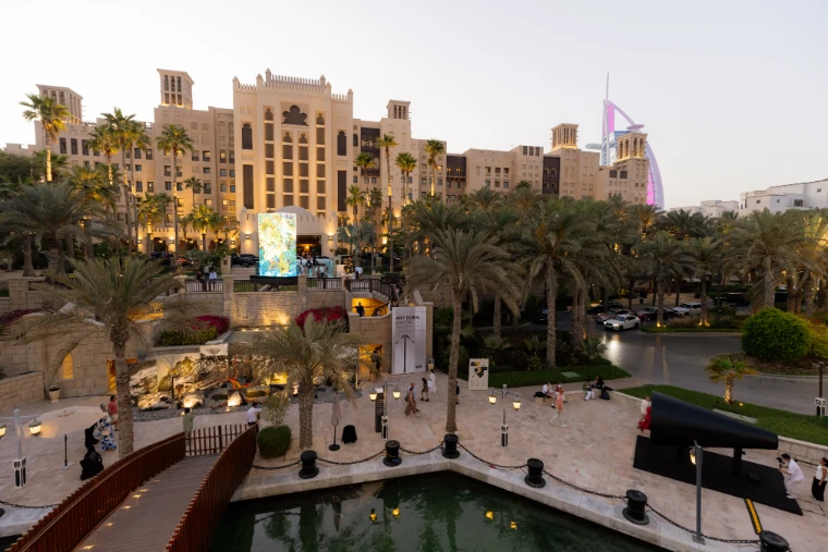 Madinat Jumeirah at dusk during Art Dubai, a digital artwork glowing before the wind-towered hotel and the Burj Al Arab beyond, a mid-April engagement in the season calendar of The Mansa Court