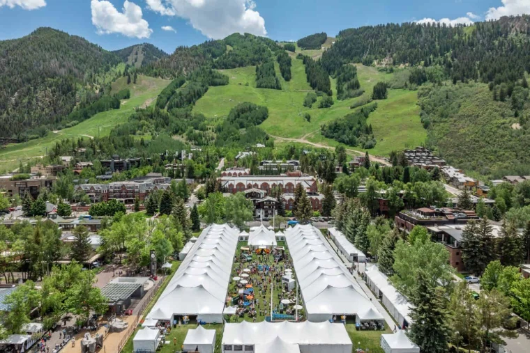 The white tasting tents of the Classic laid out in Wagner Park beneath the green slopes of Aspen Mountain, seen from above, at the Aspen Food and Wine Classic, a mid-June engagement in the season calendar of The Mansa Court