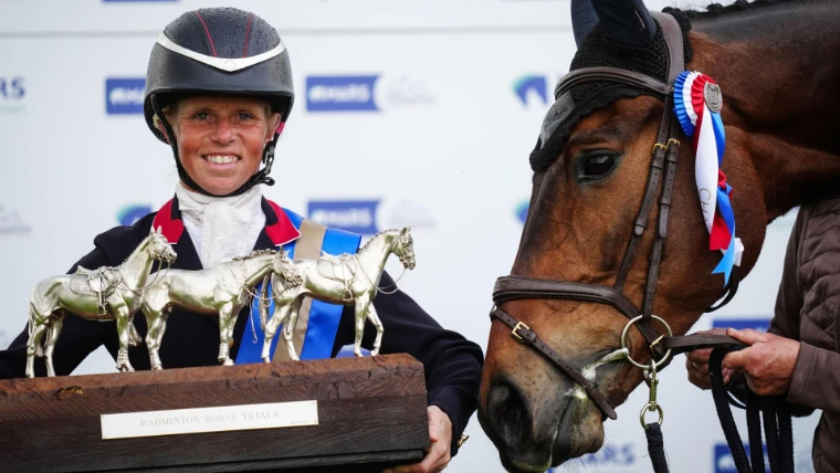 The winning rider holds the silver horse trophy beside her bay, a champion’s rosette on his bridle. Badminton Horse Trials, Gloucestershire, in the season calendar of The Mansa Court
