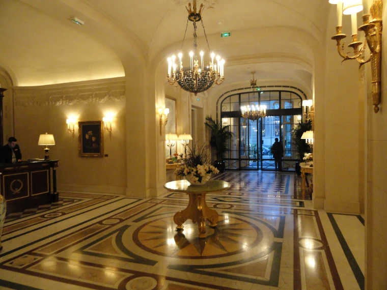 The marble-floored lobby of the Shangri-La Paris, lit by chandeliers and wall sconces, a round table of white flowers at its centre (2014).