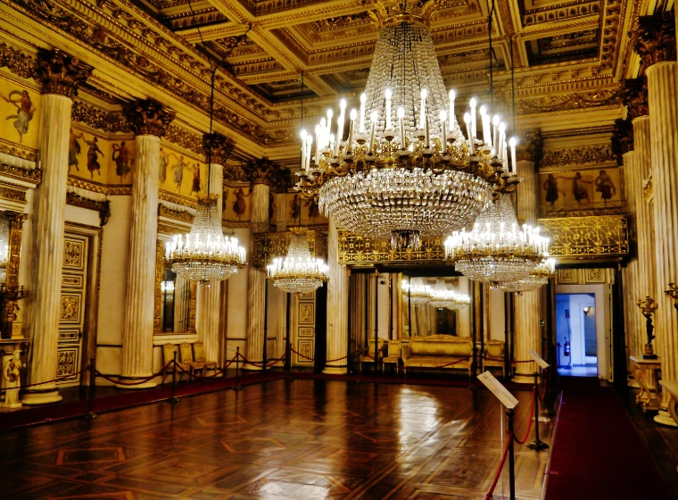 The gilded ballroom of the Royal Palace of Turin, crystal chandeliers blazing above a polished parquet floor between marble columns (2020).