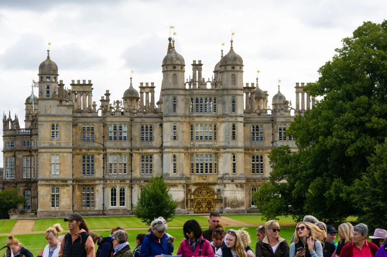 The domed and turreted front of Burghley House rises above a line of spectators on the lawn (2019).