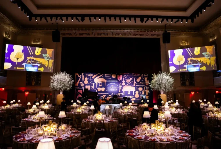 Candlelit round tables and white floral urns fill the gala dinner room, the stage dressed in Carnegie Hall’s colours. Carnegie Hall Opening Night Gala, New York, in the season calendar of The Mansa Court