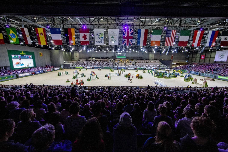 The indoor arena at Palexpo during the Rolex Grand Prix, national flags hung above a full house and the course of jumps on the sand (2018).