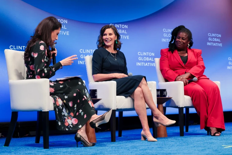 Three women in conversation in white armchairs on a blue-lit stage during the Leaders Stage session “Backing the Builders”, whose listed participants included Michigan Governor Gretchen Whitmer (23 September 2026).