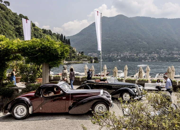 A streamlined pre-war coupe and a black cabriolet on the lakefront terrace, the water and hills behind. The Concorso d’Eleganza Villa d’Este on Lake Como, in the season calendar of The Mansa Court