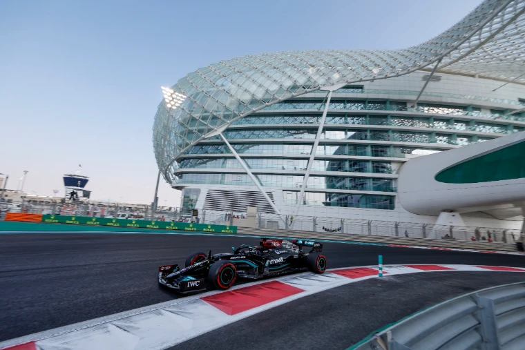 A black Mercedes Formula One car rounds a corner beneath the curving lattice canopy of the hotel that spans the track, in soft evening light (2021).