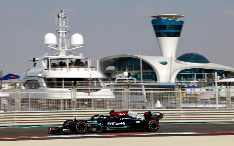 A black Mercedes Formula One car passes a large white motor yacht moored at the marina, with the marina’s control tower behind (2021).