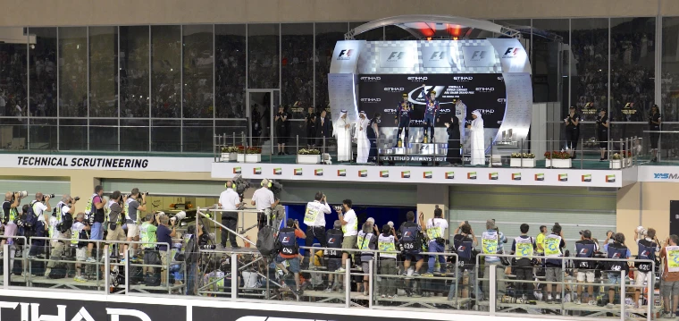 Drivers and officials on the lit podium after the race at night, with photographers crowded on the stand below (2013).