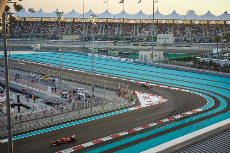 A red Formula One car takes a sweeping corner on the turquoise-edged circuit in late-afternoon light, beneath a full grandstand with a white tented roof (2013).