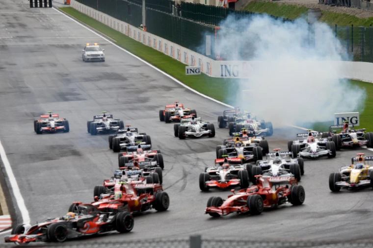 Formula 1 cars bunch together on the opening lap as a cloud of white tyre smoke rises beside the track ahead of them (2008).