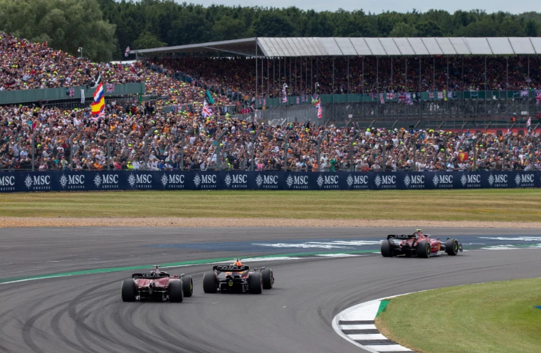 Two Ferraris and a Red Bull through a bend before packed grandstands (2022).