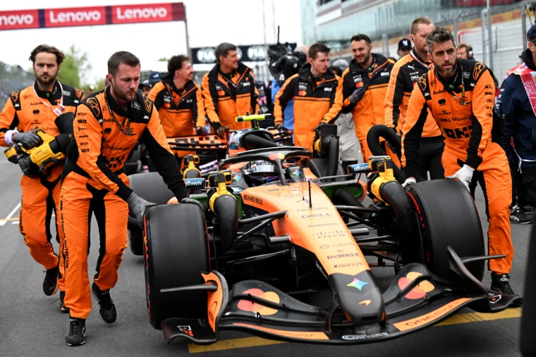 Mechanics in papaya overalls wheel a car to its place on the grid before the start. The Formula 1 Canadian Grand Prix at the Circuit Gilles Villeneuve, Montreal, in the season calendar of The Mansa Court