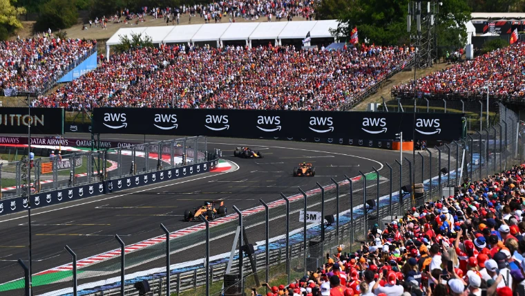 Cars sweep through a bend before packed grandstands on a summer afternoon. Formula 1 Hungarian Grand Prix, Hungaroring, Mogyoród, in the season calendar of The Mansa Court