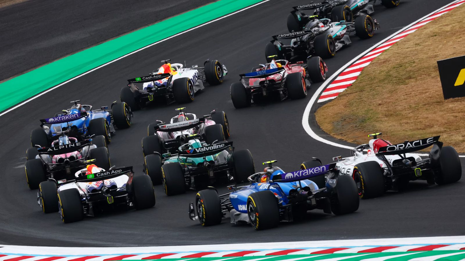 The field fanning out through the opening corners at the Formula 1 Japanese Grand Prix, Suzuka Circuit, attended by members of The Mansa Court