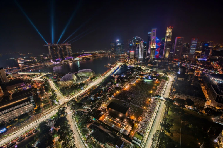 An aerial night view of the floodlit street circuit winding past the Padang and the Esplanade, with searchlights over Marina Bay Sands and the lit towers of the city behind (2012).