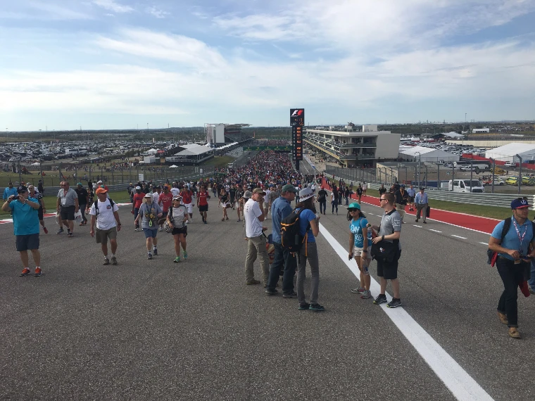Spectators streaming along the start straight after the race, the main grandstand and timing tower in the distance (2016).