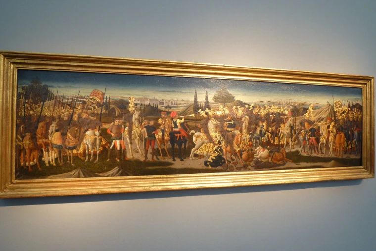 A long early Italian panel painting of a cavalcade of soldiers and horsemen hangs in a gilt frame on a pale grey-blue wall at Frieze Masters (2012).