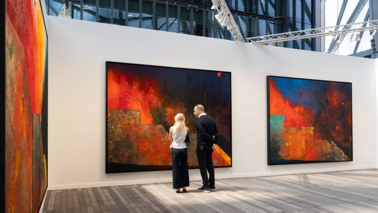 Two visitors stand before a wall of large abstract canvases in red, orange and blue beneath the glazed roof of The Shed. Frieze New York at The Shed, Hudson Yards, in the season calendar of The Mansa Court