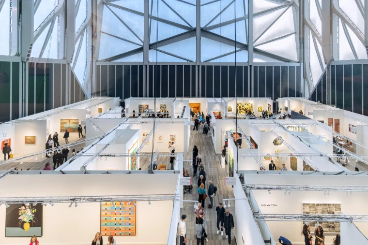 The fair seen from above, its white booths and aisles filled with visitors under the steel and glass of The Shed. Frieze New York at The Shed, Hudson Yards, in the season calendar of The Mansa Court