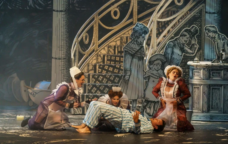 Three maids in Edwardian costume gather round a fallen figure against a drawn black-and-white set. Glyndebourne Festival Opera, near Lewes in East Sussex, in the season calendar of The Mansa Court