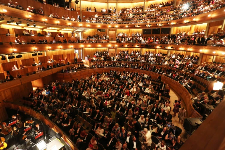 A full house in black tie fills the wooden tiers of the opera house above the orchestra pit before curtain up. Glyndebourne Festival Opera, near Lewes in East Sussex, in the season calendar of The Mansa Court