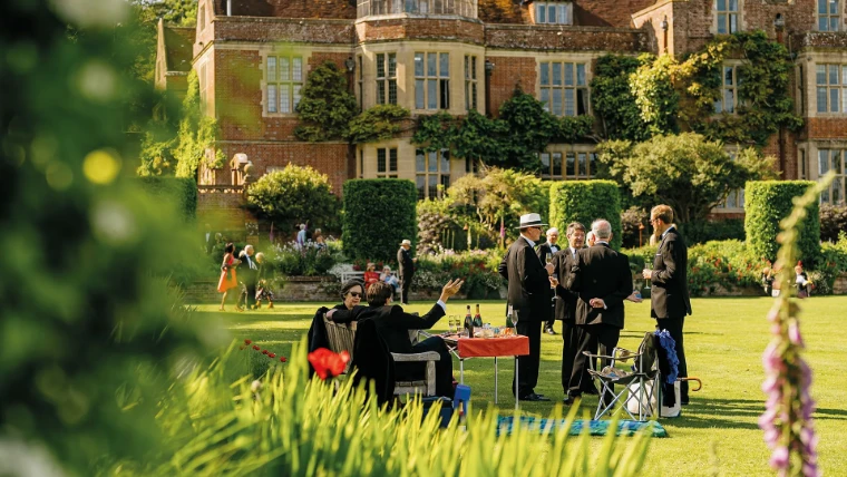 Guests in black tie picnic with champagne on the lawn before the old house during the long interval. Glyndebourne Festival Opera, near Lewes in East Sussex, in the season calendar of The Mansa Court