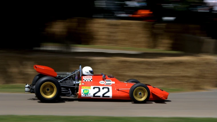 An orange vintage single-seater racing car numbered 22 speeds along the hillclimb course past straw bales, the background blurred by motion (2008).