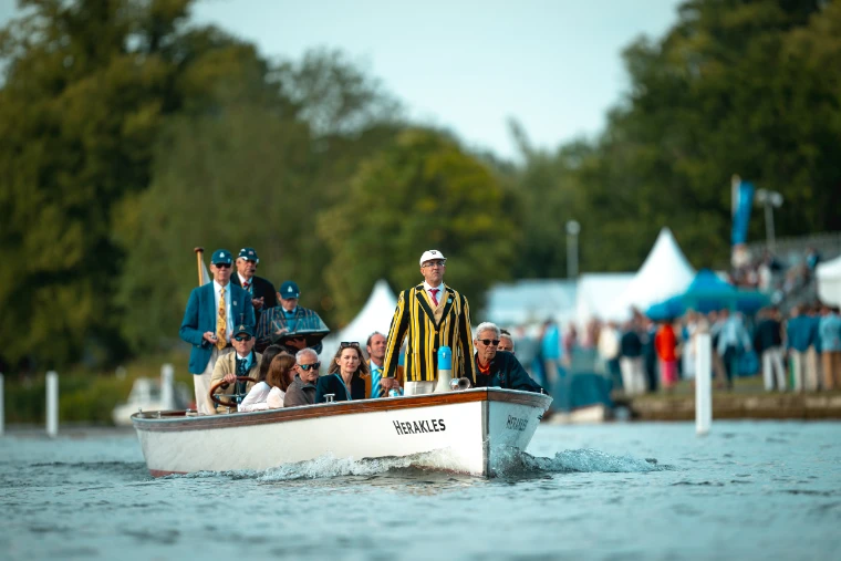 The umpire’s launch Herakles follows a race, officials in blazers aboard, one in a striped blazer and white cap.