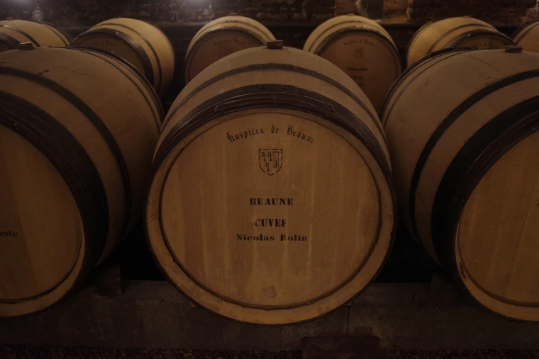 Oak barrels stacked in a cellar of the Hospices de Beaune, the one in front stencilled “Hospices de Beaune”, “Beaune” and “Cuvée Nicolas Rolin” (2025).