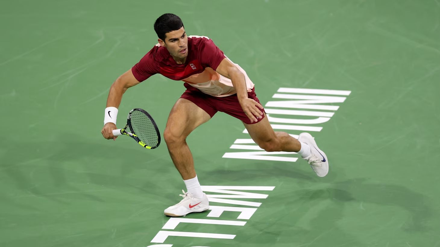 A player reaching across the green court under the lights at Indian Wells, the fortnight of tennis The Mansa Court attends each March in the California desert