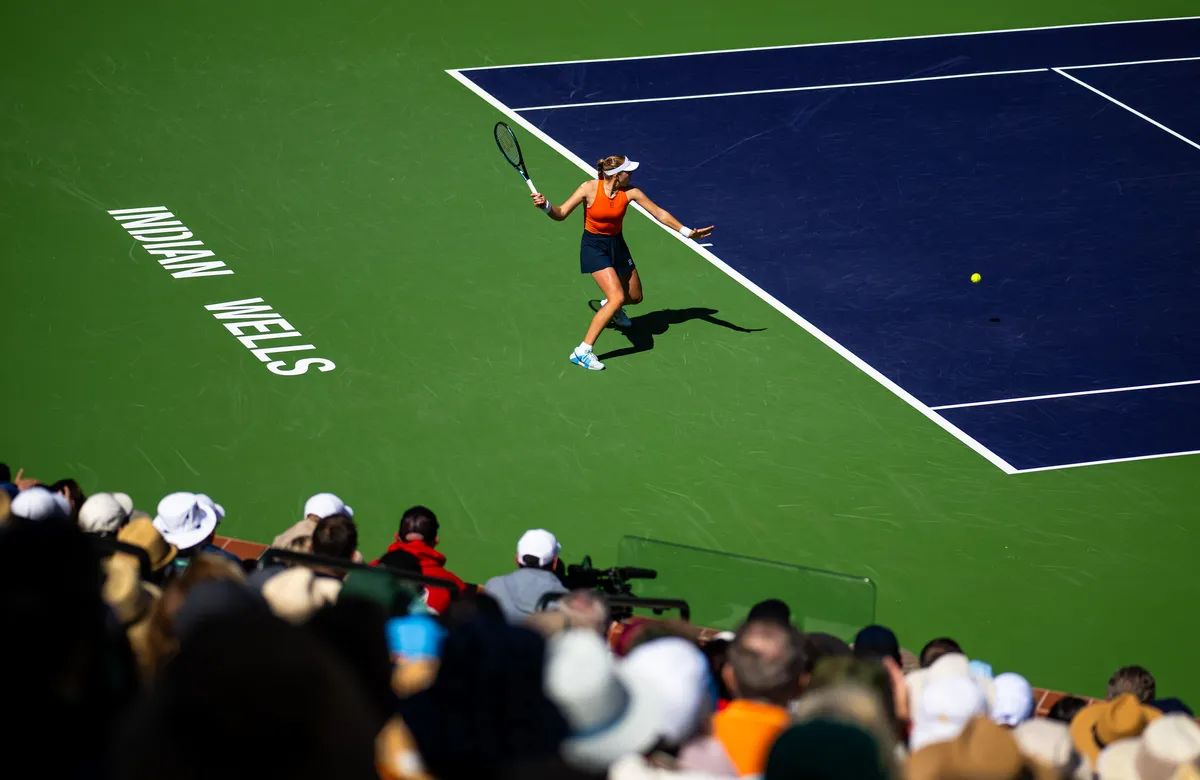 A player striking a forehand on the stadium court with INDIAN WELLS painted on the green at the BNP Paribas Open, the fortnight of desert tennis The Mansa Court keeps each March