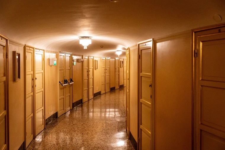 A curving corridor of numbered box doors lit by a ceiling lamp, with a polished terrazzo floor (2023).