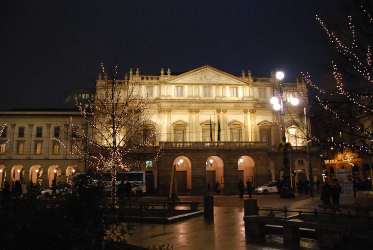 The facade of the Teatro alla Scala floodlit at night in December, with trees strung with white lights in the wet piazza in front (2008).