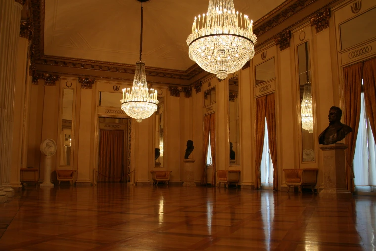 A foyer of La Scala with crystal chandeliers, tall curtained windows, marble busts and a polished parquet floor (2007).