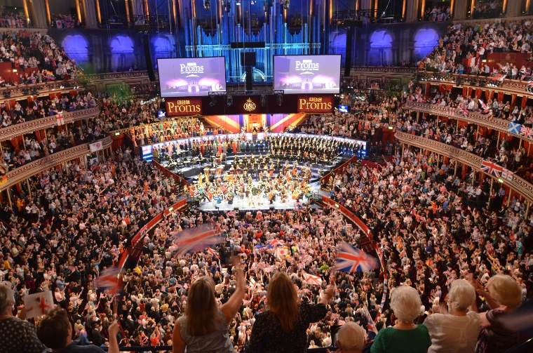 The packed Royal Albert Hall seen from high up, with flags waving in the Arena and the orchestra and chorus on the platform beneath the organ (2014).