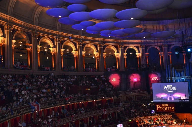 The blue-lit acoustic discs under the dome of the Royal Albert Hall above the arched Gallery and the filling tiers of seats (2014).