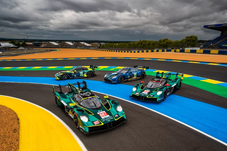 Aston Martin hypercars and GT cars posed on the painted kerbs of the Circuit de la Sarthe beneath a heavy sky, at the Le Mans 24 Hours, the June race in the season calendar of The Mansa Court