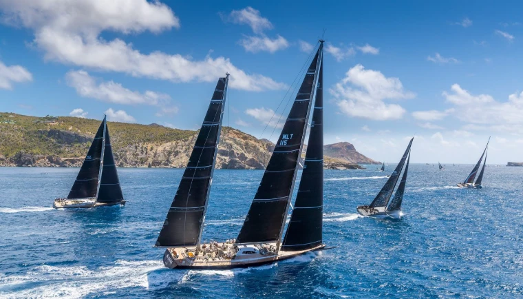 Maxi yachts under black sails racing past the rocky coast at Les Voiles de Saint-Barth, a mid-April engagement in the season calendar of The Mansa Court