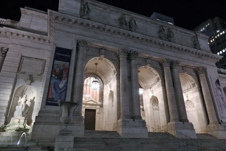 The Library’s Fifth Avenue portico of marble columns and arches, lit at night above its steps (2022).