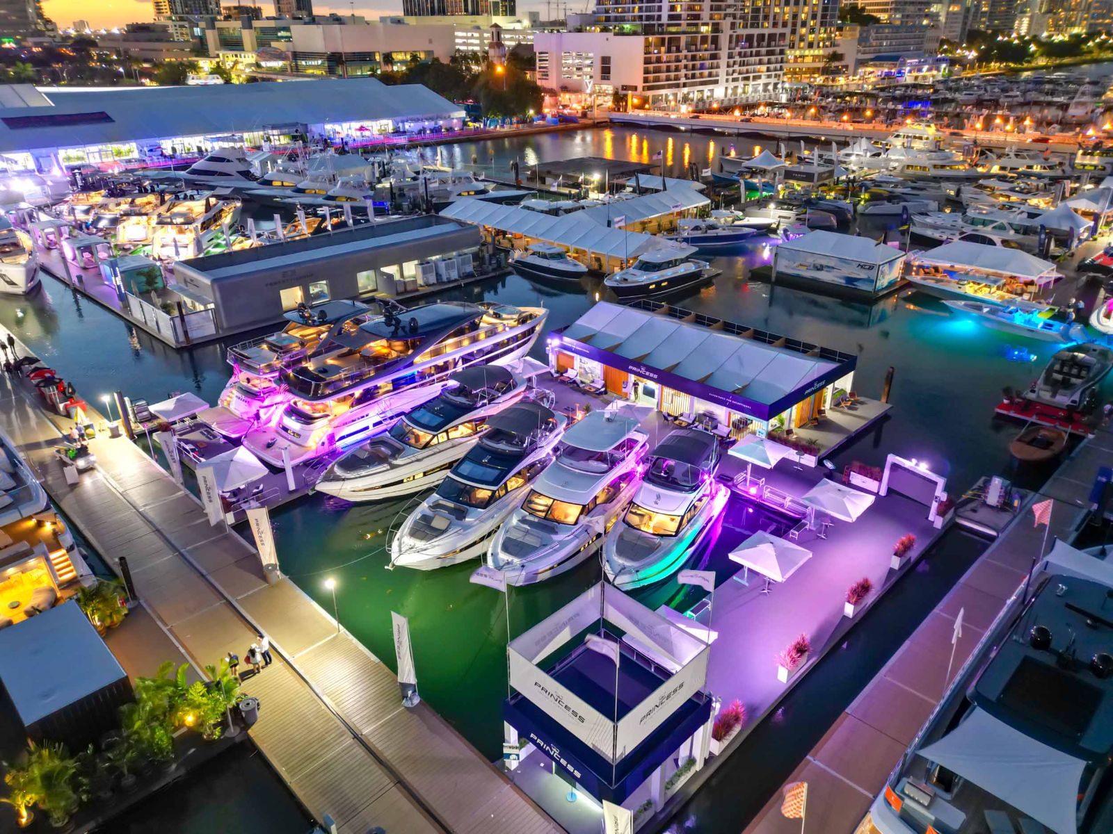 An aerial view of the show marina at dusk with motor yachts berthed in ranks under coloured light at the Miami International Boat Show
