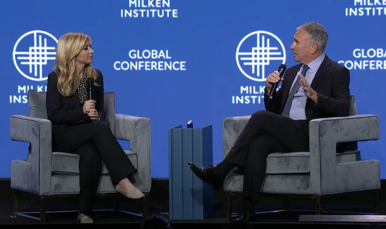 Two speakers in grey armchairs talk before the blue Global Conference screen. The Milken Institute Global Conference at The Beverly Hilton, Beverly Hills, in the season calendar of The Mansa Court