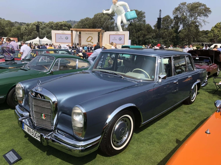 A grey-blue Mercedes-Benz 600 limousine is parked on the lawn at The Quail among other classic cars, with a crowd and white pavilions behind (2018).