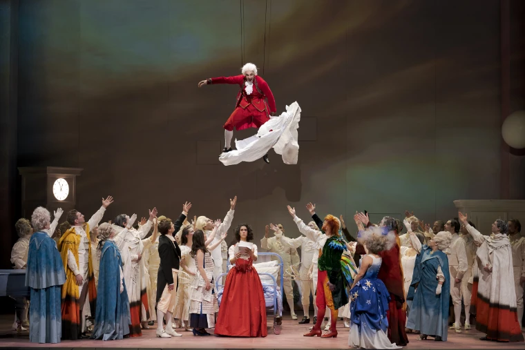 A Mozart figure in a red coat flies above the cast of Die Zauberflöte at the Mozartwoche (2026). Mozartwoche, Haus für Mozart, Salzburg, in the season calendar of The Mansa Court
