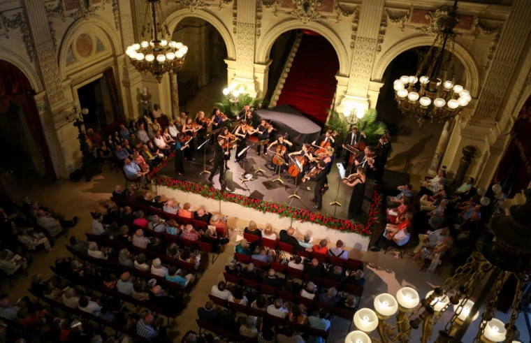 A chamber orchestra plays in the Great Hall of The Breakers, the audience seated beneath its chandeliers. Newport Classical Music Festival, The Breakers, Newport, Rhode Island, in the season calendar of The Mansa Court